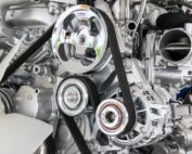 Ein silberner Motorblock mit Metallrädern, auf denen schwarze Keilriemen laufen.
