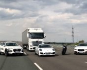 Drei weiße Autos, in Motorrad und ein Lkw stehen auf einer Straße.